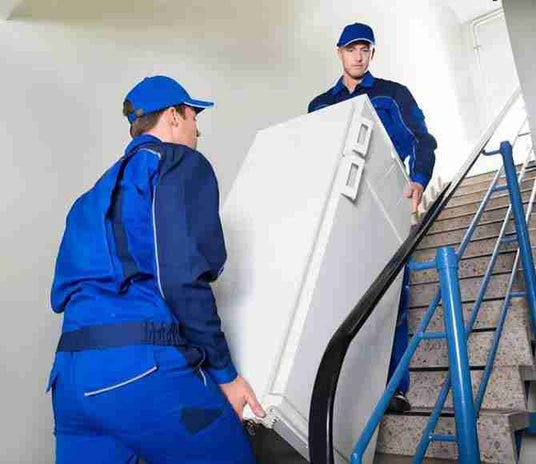Appliance delivery service carrying a refrigerator up the stairs for installation and haul away old appliance.